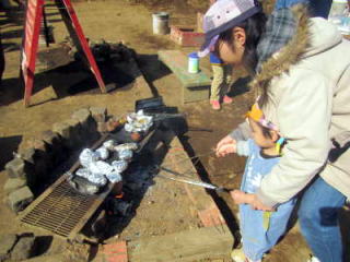 （写真）たき火で焼き芋を焼く親子